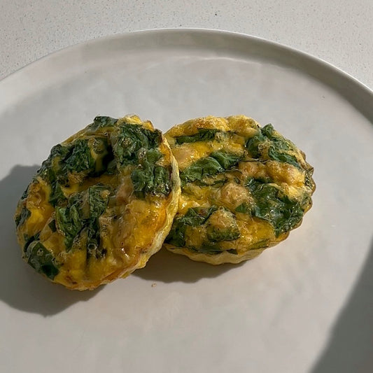 A plate of two circular dog-friendly egg bites arranged on a plate. They feature eggs, spinach, and ground turkey.