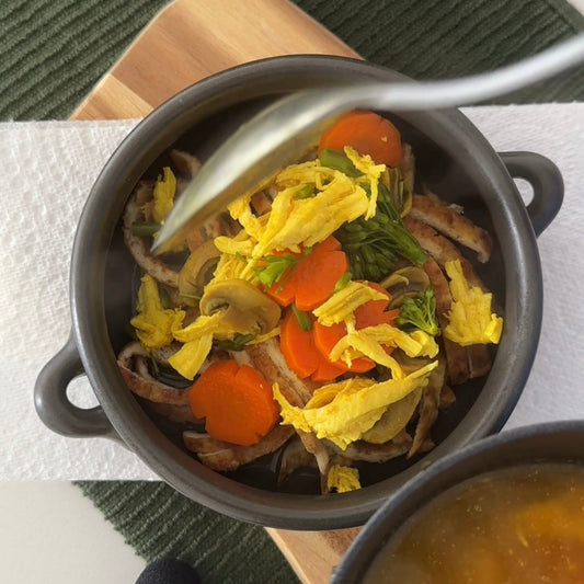 A small gray pot of dog-friendly chicken noodle soup featuring eggs and various vegetables. A Spo